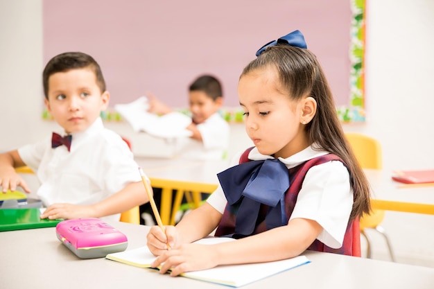 Élèves préscolaires mignons portant un uniforme et faisant un devoir d'écriture dans une salle de classe