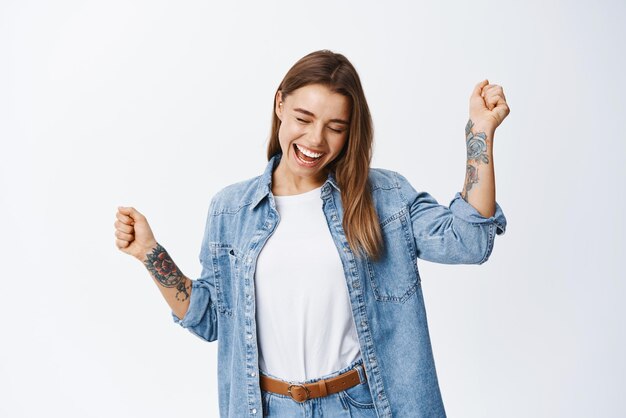 Liberté et bonheur Femme insouciante s'amusant à danser fermer les yeux et sourire tout en se relaxant avec de la musique debout optimiste sur fond blanc