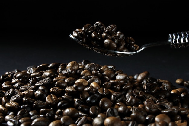 Libre d'une cuillère tenant des grains de café fraîchement torréfiés sur un fond sombre