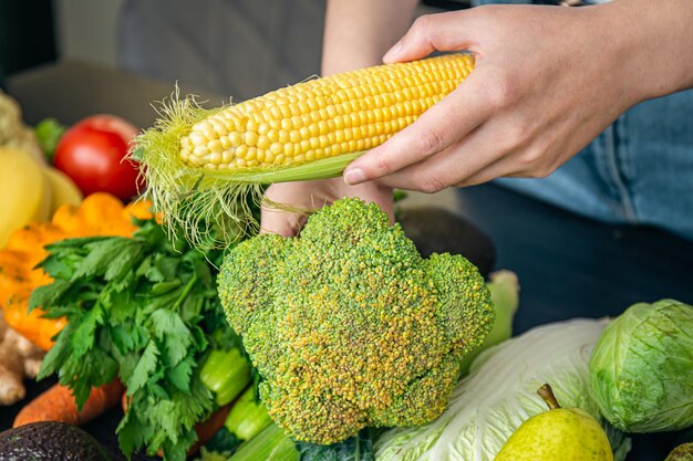 Libre de maïs dans les mains des femmes et autres légumes sur la table de la cuisine