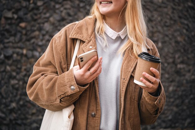 Libre une tasse de café et un smartphone dans les mains des femmes dans la ville