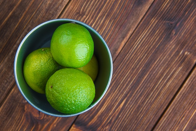 Limes dans un mini seau sur une table en bois. pose à plat.