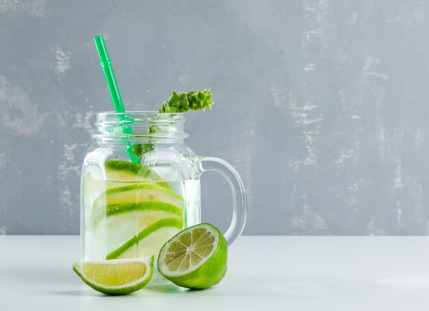 Limonade au citron, herbes dans un bocal en verre sur fond blanc et plâtre,