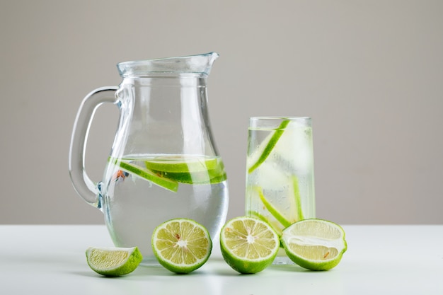 Limonade en verre et cruche avec vue latérale citrons sur blanc et gris