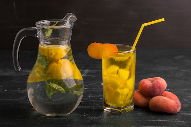 Photo gratuite limonade en verre et pot avec des pêches autour isolé sur une surface noire