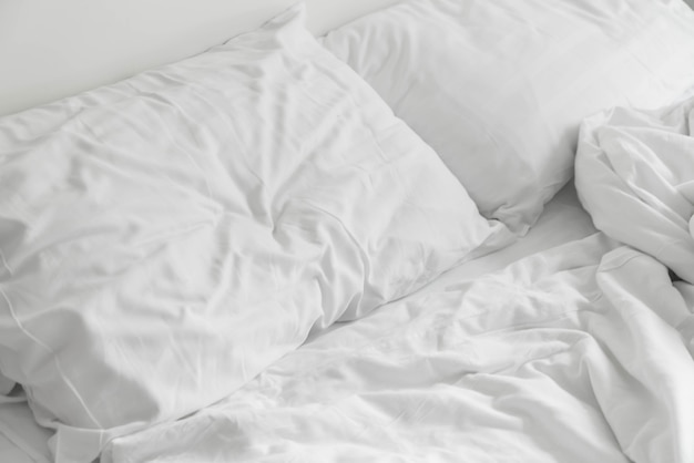 Lit froissé avec une décoration d&#39;oreillers en désordre blanc dans la chambre à coucher
