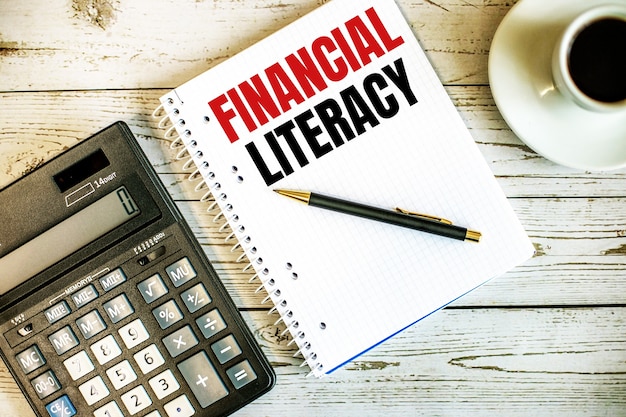 Littératie financière écrite sur du papier blanc près de café et calculatrice sur une table en bois clair