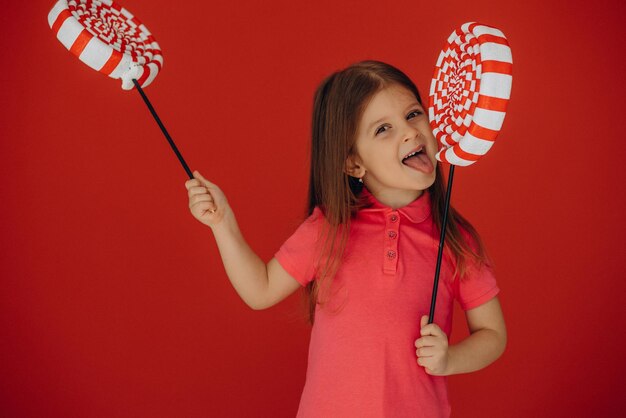 Little girl holding big lollypop isolé sur fond rouge