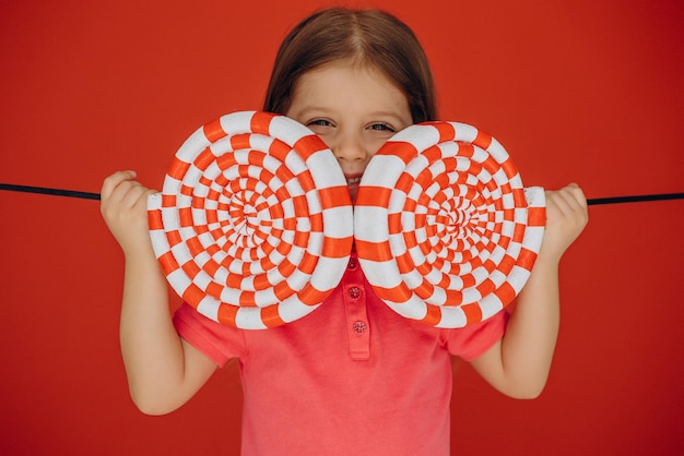 Little girl holding big lollypop isolé sur fond rouge