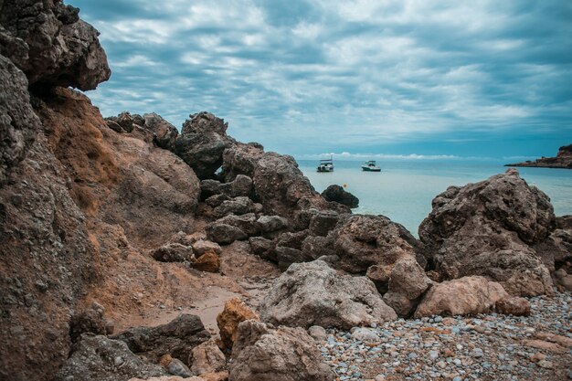 Littoral plein de rochers, quelques navires dans la mer et le ciel nuageux