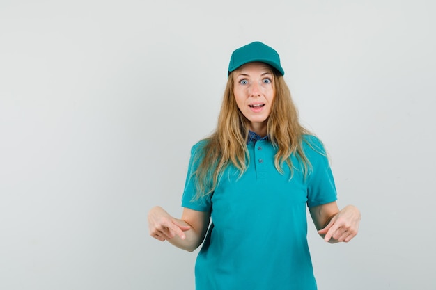 Livraison femme pointant vers le bas en t-shirt, casquette et à la surprise