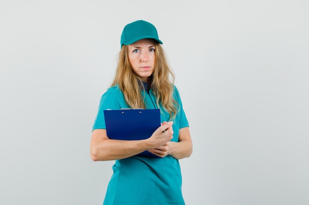 Livraison femme en t-shirt, casquette tenant le presse-papiers et à la recherche sensible