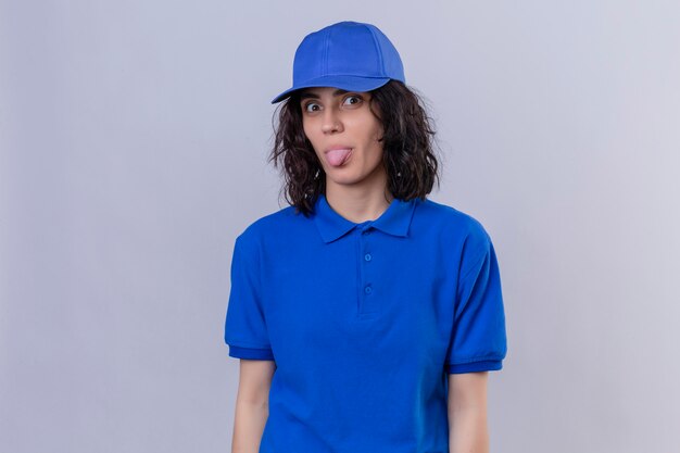 Photo gratuite livraison fille en uniforme bleu et cap sticking tongue out heureux avec drôle d'expression debout sur blanc isolé