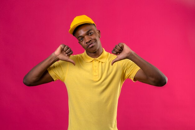 Livraison homme afro-américain en polo jaune et casquette à la confiance pointant vers lui-même fier debout sur rose