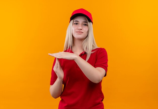 Livraison jeune femme portant un t-shirt rouge et une casquette montrant le geste de délai d'attente sur un mur orange isolé