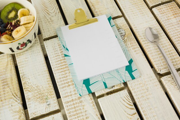 Livre blanc sur le presse-papiers avec cuillère et bol de salade de fruits sur fond en bois