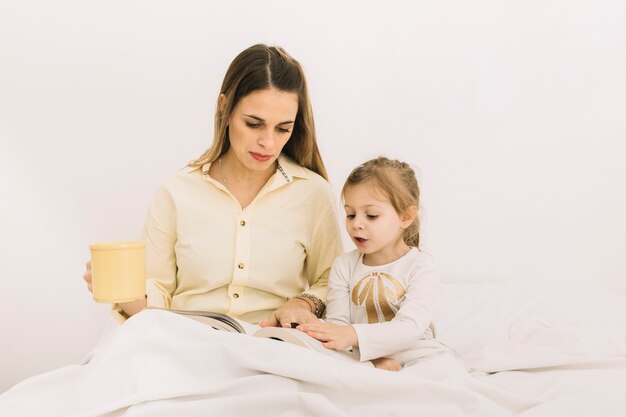 Livre de lecture de fille étonnée avec mère au lit