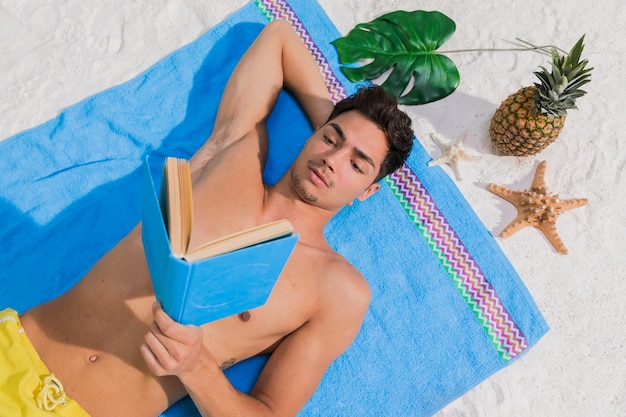 Photo gratuite livre de lecture séduisante jeune homme sur la plage