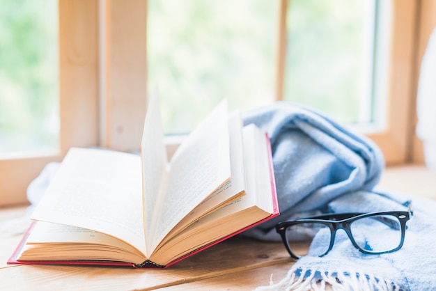 Livre ouvert, lunettes et couverture bleue près de la fenêtre