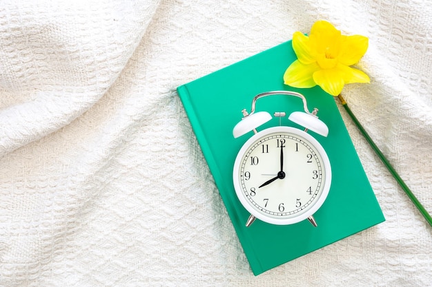 Photo gratuite livre réveil et fleur en vue de dessus de lit blanc