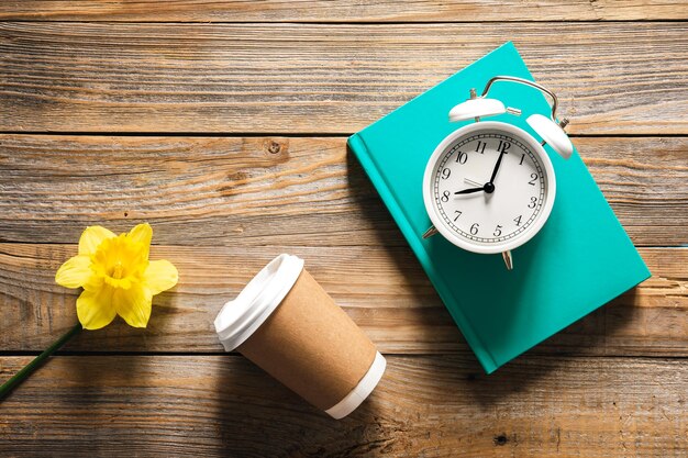 Photo gratuite livre réveil papier tasse et fleur sur la vue de dessus de fond en bois