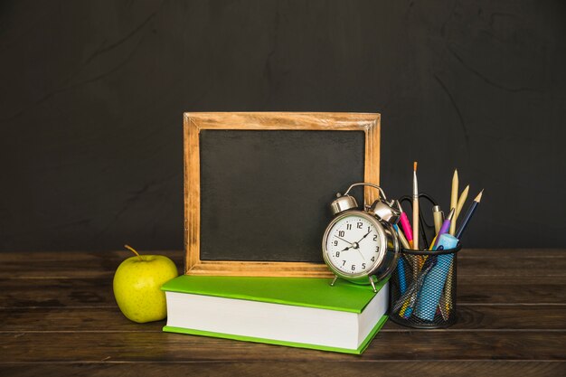 Livre avec tableau noir et réveil sur table avec papeterie