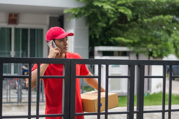 Livreur avec colis appelant un client devant la maison.