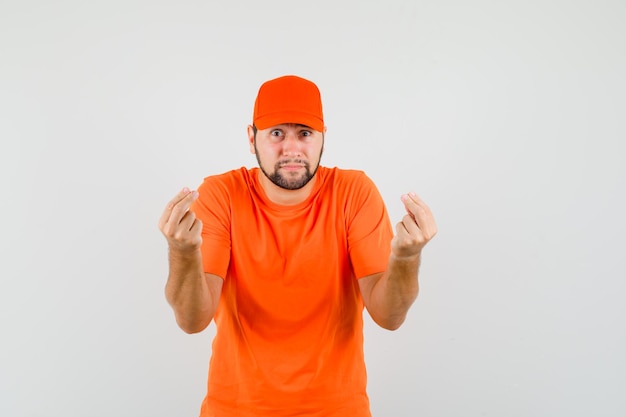 Photo gratuite livreur faisant des gestes avec deux doigts en t-shirt orange, casquette et semblant anxieux, vue de face.