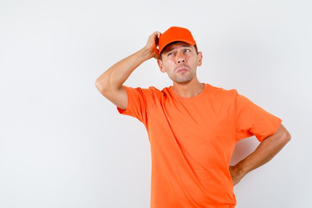 Livreur de gratter la tête en t-shirt et casquette orange et à la pensif