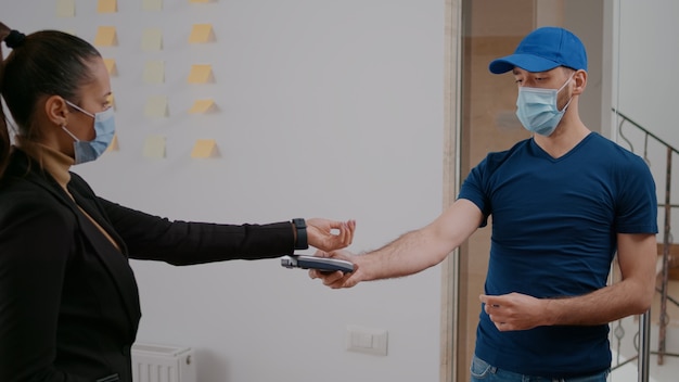 Livreur avec masque de protection et gants livrant une boîte de plats à emporter pendant l'heure du déjeuner au bureau de l'entreprise