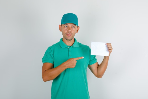 Livreur montrant enveloppe avec doigt en t-shirt vert avec casquette