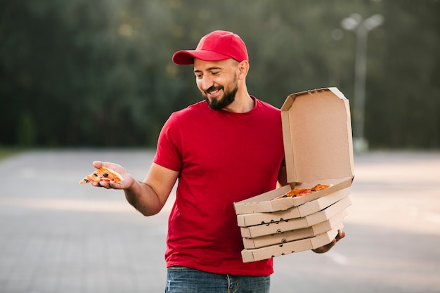 Livreur moyen de tir regardant une tranche de pizza