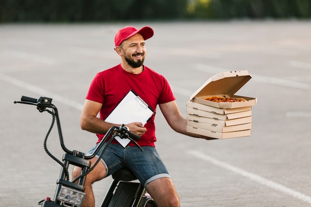 Photo gratuite livreur à moyen tirage brandissant des boîtes avec une pizza