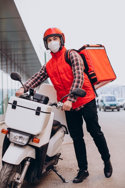 Livreur de nourriture conduisant un scooter avec une boîte avec de la nourriture et portant un masque