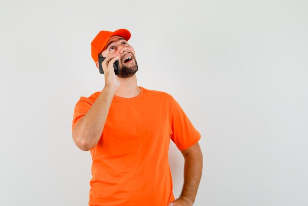 Livreur parlant sur téléphone portable en t-shirt orange, casquette et espoir, vue de face.