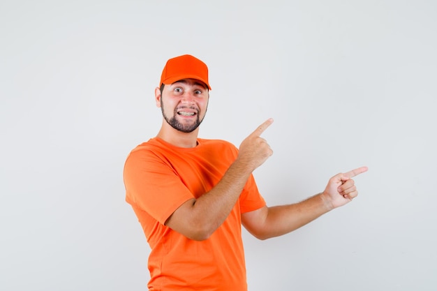 Livreur Pointant Sur Le Côté Avec Le Doigt Vers Le Haut En T-shirt Orange, Casquette Et Semblant Joyeux. Vue De Face.