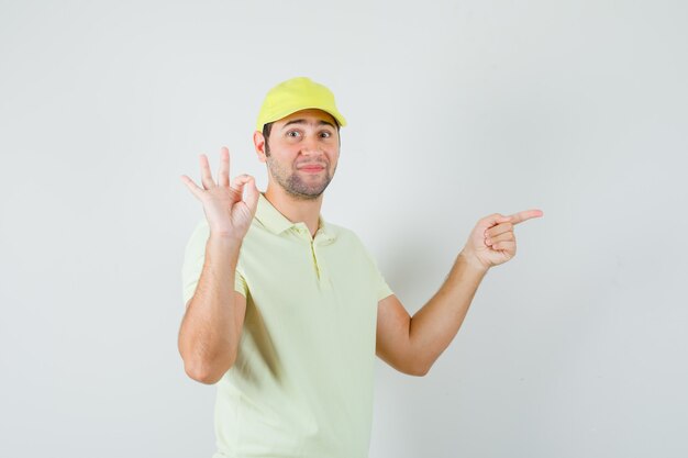 Livreur pointant de côté, montrant signe ok en uniforme jaune et à la confiance. vue de face.