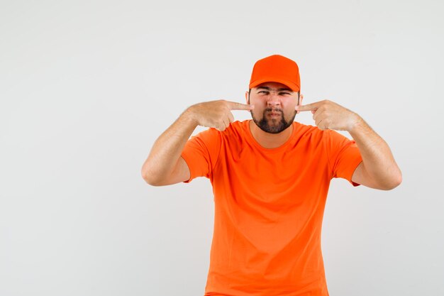 Photo gratuite livreur pointant sur sa moustache en t-shirt orange, casquette, vue de face.