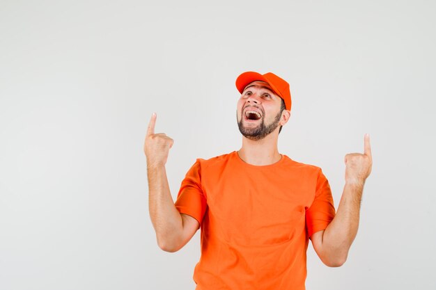 Livreur pointant vers le haut en t-shirt orange, casquette et semblant heureux. vue de face.