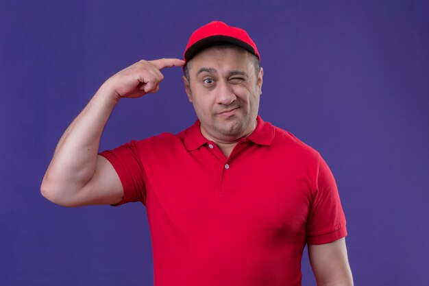 Livreur portant un uniforme rouge et une casquette à la confusion de se gratter la tête ayant des doutes debout