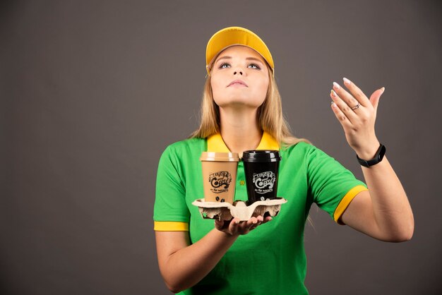 Livreur reniflant des tasses de café sur un mur noir.