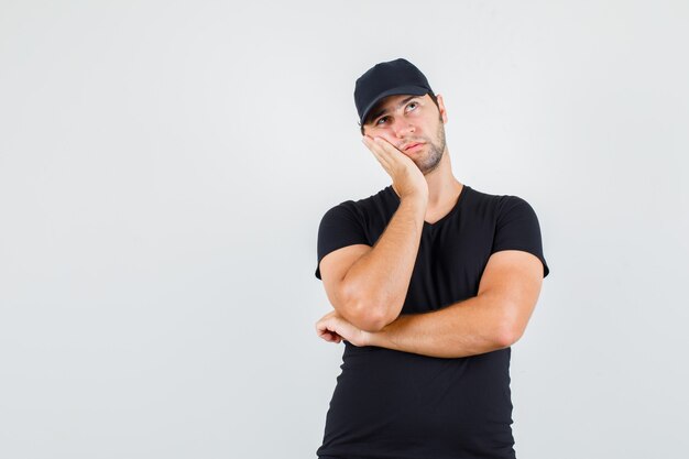 Livreur en t-shirt noir, casquette penchée sur la joue sur la paume surélevée et à la pensif