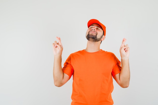 Livreur en t-shirt orange, casquette gardant les doigts croisés et l'air paisible, vue de face.