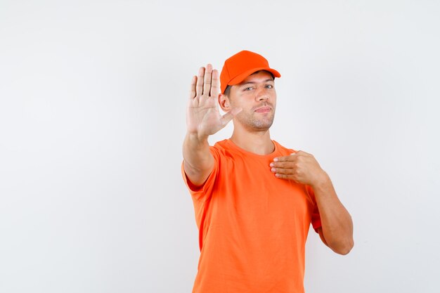 Livreur en t-shirt orange et casquette montrant le geste d'arrêt en pointant sur lui-même et à la confiance