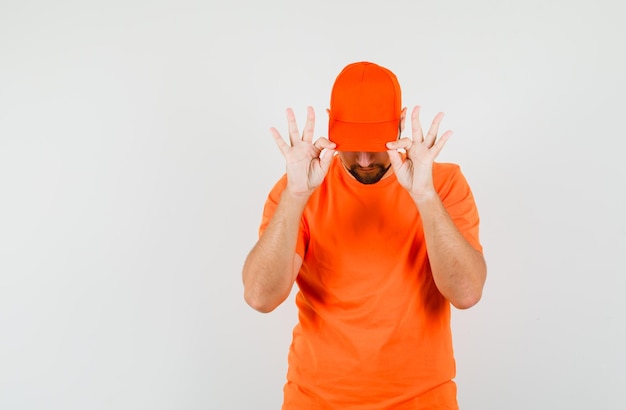 Photo gratuite livreur en t-shirt orange tirant vers le bas le capuchon sur ses yeux et l'air cool, vue de face.