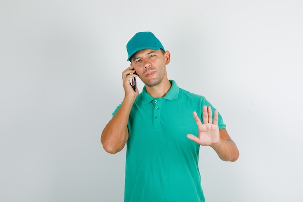 Livreur en t-shirt vert avec casquette parlant au téléphone avec panneau d'arrêt