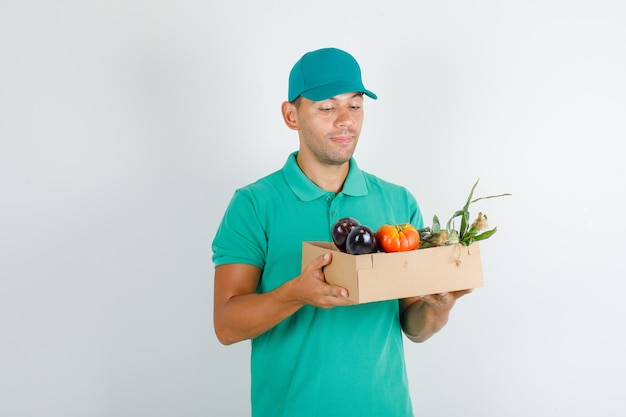 Livreur en t-shirt vert et casquette tenant des légumes dans une boîte et à la bonne humeur