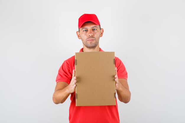 Livreur tenant une boîte en carton en uniforme rouge. vue de face.