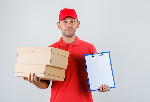 Livreur tenant des boîtes en carton et presse-papiers en vue de face uniforme rouge.