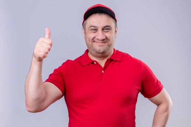 Livreur en uniforme rouge et chapeau avec visage heureux montrant les pouces vers le haut debout sur un espace blanc isolé